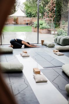 a woman is doing yoga in front of a large glass window with lots of pillows on the floor