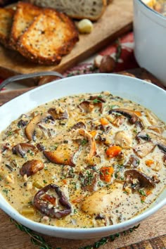 a white bowl filled with mushroom soup next to bread on a cutting board and serving utensils