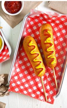 two hotdogs with mustard and ketchup on a red and white checkered tablecloth