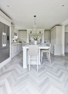 a large kitchen with white cabinets and an island in the middle is decorated with gray herringbone tile