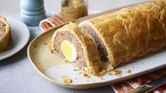 a meatloaf roll with an egg in the middle on a plate next to other food items