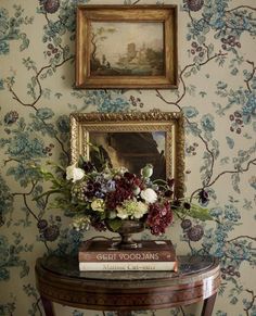 a table with flowers and books on it in front of a wallpapered wall