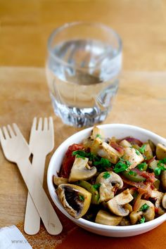 a white bowl filled with food next to a fork and glass on top of a wooden table