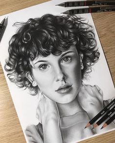 a pencil drawing of a woman's face with curly hair and blue eyes on a wooden table