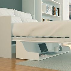 a white bed with a laptop on it under a book shelf next to a couch