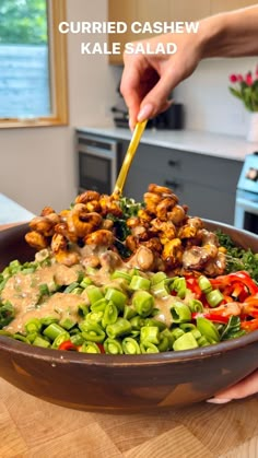 a person is holding a wooden spoon over a bowl filled with vegetables and meats