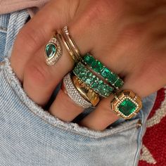 a close up of a person's hand with rings on their fingers and emeralds