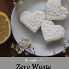 four heart shaped marshmallows on a white plate next to an orange slice