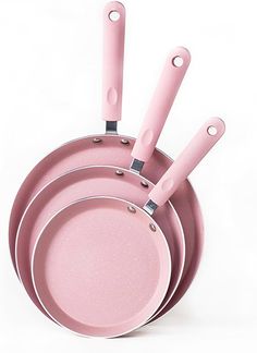 three pink pans with handles on each side and one has two spoons in the middle