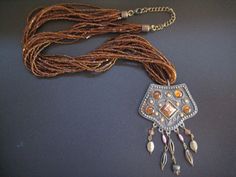 This is a large bronze colored pendant hanging on a 26" ten stranded amber seed bead necklace.  The pendant is embellished with amber-like resin stones and has five dangles at the bottom, some with topaz colored glass beads and some with purple pearl-like beads.  The necklace has a lobster clasp and a 3" curb chain extension making it a total of 29" long.  The pendant measures 3 3/4" long including the bale and dangles and is 2 3/8" wide. Topaz Color, Purple Pearl, Seed Bead Necklace, Curb Chain, Bronze Color, Bling Bling, Bead Necklace, Seed Bead, Colored Glass