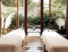 two white beds sitting next to each other in a room with wooden floors and large windows