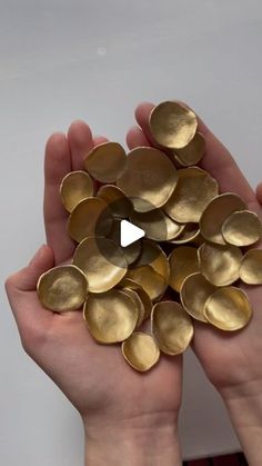 two hands holding gold discs in front of a white wall