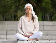 a woman sitting in a lotus position with her eyes closed while wearing a white head scarf