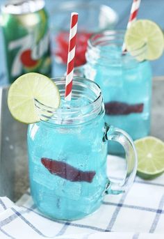 two mason jars filled with blue liquid and lime slices on a tray next to cans of soda