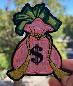 a hand holding up a pink bag with a dollar sign on it and a green bow