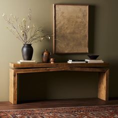 a wooden table with vases and books on it in front of a framed painting