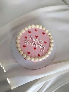 a pink birthday cake with white and red frosting on it's side sitting on a bed