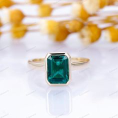 an emerald colored stone sits on top of a gold ring with flowers in the background