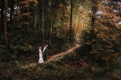 a bride and groom standing on a path in the middle of a forest, surrounded by trees