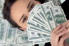 a woman hiding her face behind stacks of money