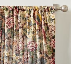 a curtain with floral print on it hanging in front of a white wall and metal rod