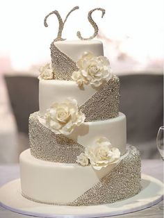 a three tiered wedding cake with white flowers on the top and silver sequins