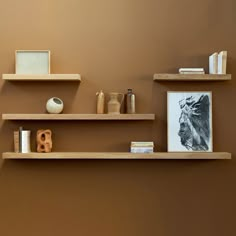 three wooden shelves with books, vases and other items on them against a brown wall