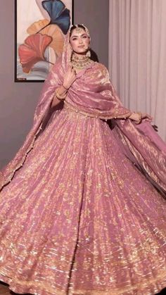 a woman in a pink and gold wedding gown standing next to a painting on the wall