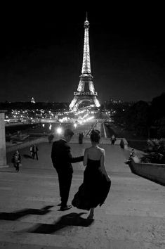 a man and woman standing in front of the eiffel tower, at night