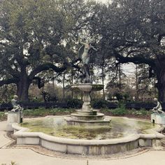 a fountain in the middle of a park surrounded by trees