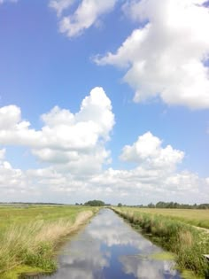 a river running through a lush green field under a blue sky with fluffy white clouds