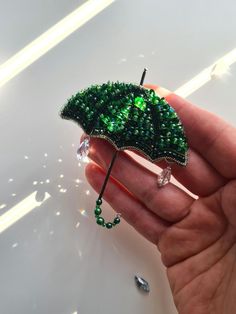 a hand holding a green beaded brooch with an umbrella shaped like a leaf