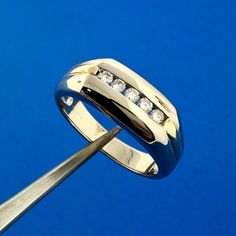 a diamond set wedding ring being held by a pair of scissors on a blue background