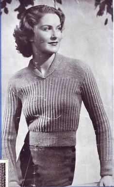 an old black and white photo of a woman wearing a knitted sweater with her hands in her pockets