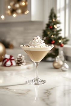 a drink in a martini glass with sprinkles on the rim and a christmas tree behind it