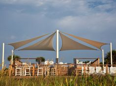 an outdoor dining area with tables and chairs under a large shade sail over it's roof