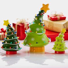 three small christmas trees sitting next to each other on top of a white table with presents