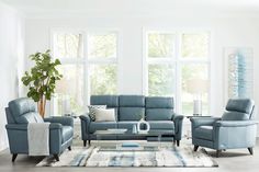 a living room filled with blue furniture and large windows in the wall behind it is a white rug