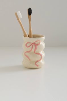 two toothbrushes in a cup with pink ribbon on the handle and white background