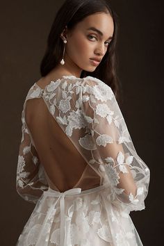 the back of a woman wearing a white dress with sheer sleeves and flowers on it