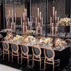 a long table is set up with black chairs and white flowers in tall vases