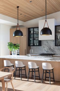 a kitchen with wooden flooring and white chairs next to an island counter top that has three pendant lights hanging from it