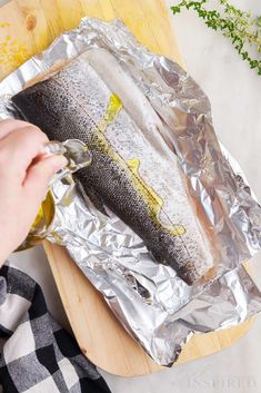 someone is holding a fish in foil on a cutting board