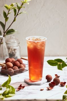 a glass filled with liquid sitting on top of a table next to some leaves and flowers