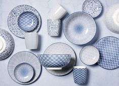 an assortment of blue and white plates, cups and saucers on a gray background