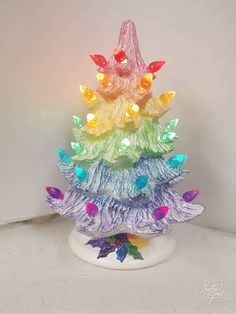 a multicolored christmas tree with lights on it's top is shown in front of a white wall