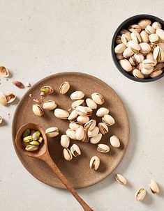 nuts are scattered on a plate next to a wooden spoon and bowl full of them