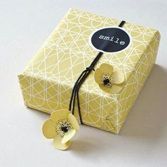 a small yellow box with two flowers on the side and a black tag that says smile