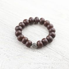 a wooden beaded bracelet with a silver skull charm on it's end, sitting on a white wood surface