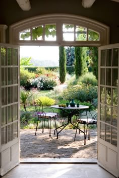 an open door leading to a patio with table and chairs on it, surrounded by greenery